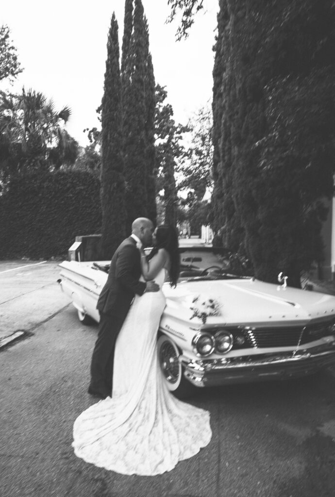 A bride and groom share a kiss in front of the classic car they rented for their Charleston, SC wedding.