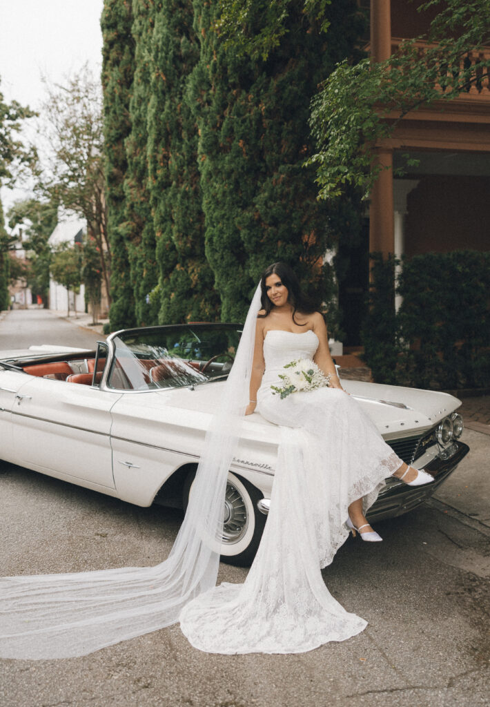 A bride poses on the classic car they rented for their Charleston, SC wedding.