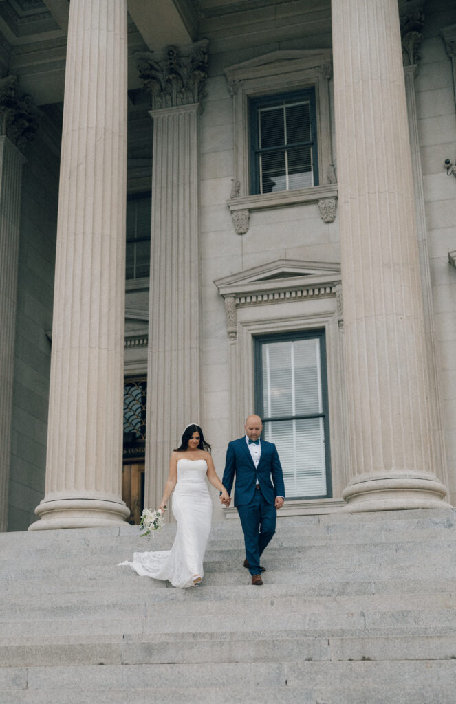 A bride and groom walking down the steps of a building in downtown Charleston, SC.