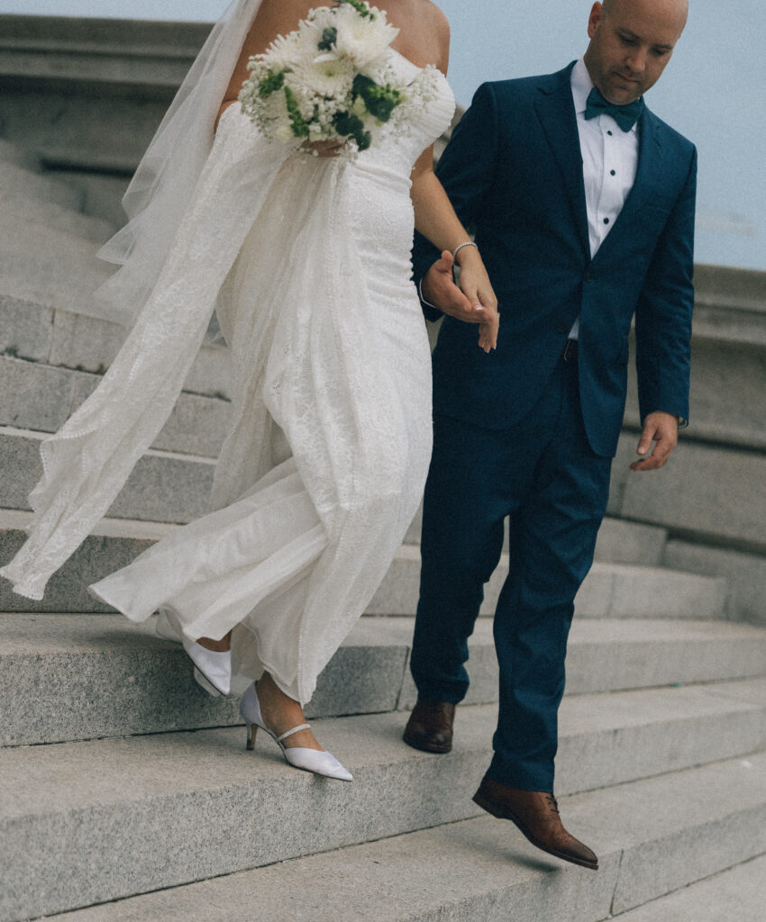 A bride and groom hand in hand on the steps of a building in downtown Charleston, SC.