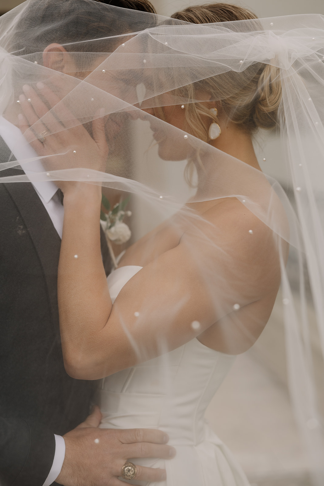 A bride and groom pose under her veil for portraits on their wedding day.